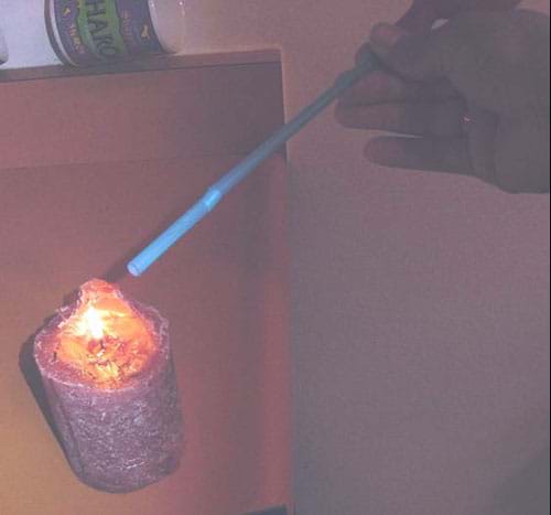 A photograph shows a tilted bottle with a straw attached to its mouth. The other end of the straw is positioned near the flame of a burning candle.