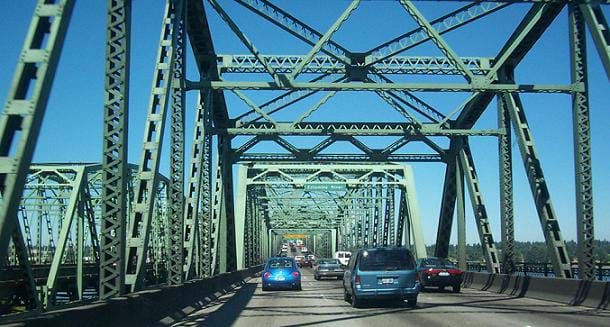 View crossing a bridge through a tunnel created by green steel truss members.