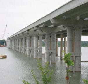 Photo shows view looking at a row of concrete columns and beams that compose a bridge over water.
