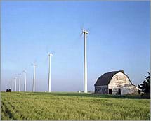 A picture showing many wind turbines with a barn in the foreground. 