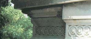 A photograph of a corner of the U.S. Capitol building, a marble structure. The leftmost portion of the corner is stained dark from acid rain.