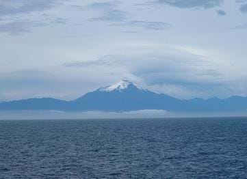 A photograph of Corcovado, a volcanic mountain. The vast sea is in the foreground, with the blue-tinted mountain in the background.
