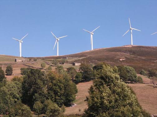 Landscape photo shows four, white, electricity-generating wind turbines on a hillside.