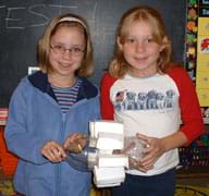 Two girls hold a two-liter plastic bottle with taped-on paper paddles.