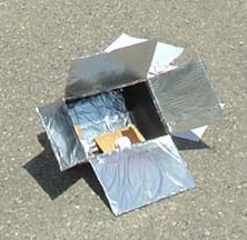 Photo shows a box with flaps covered in foil, and chocolate, marshmallow and graham cracker inside the box.
