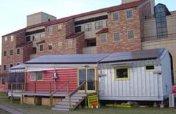 Photograph of a modern mobile-home-size structure in front of a huge university building.
