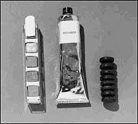 A photograph of astronaut's food from Project Mercury, showing a food tube and bite-sized snacks. The tube looks like a toothpaste tube, and one of the snacks looks like a small stack of eight mini-car tires. The other snack appears to be a set of small cubes placed in a metal holder. 
