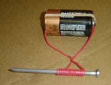 Photo shows a nail wrapped in red wire with the wire ends connected with a rubber band to opposite ends of a D-cell battery.