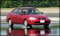 Photograph of a red sedan stopping on a wet road surface, showing a splash of water below the front wheels.