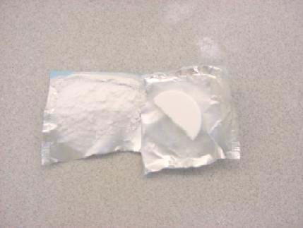 A photograph of an antacid tablet placed on its open wrapper. On the right is a solid half of one tablet. On the left, the other half is crushed into a powder.