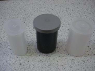 A photograph comparing three types of film canisters. The canister on the left is translucent and elliptical in shape. The canister in the center is black with a gray overlapping cap and is used for 35 mm film. The canister on the right is also for 35 mm film but is translucent and has a different fitting cap.