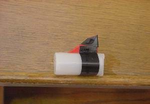 A photograph showing a film canister with a red keel adhered to it with black electrical tape.