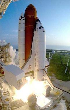 A photograph of NASA's Space Shuttle Discovery as it prepares for its ascent into space. The external fuel tank, orbiter and solid rocket boosters are visible.