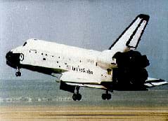 Photo shows a US space shuttle landing, with its rear wheels about to touch the runway and its nose and front wheels still in the air.
