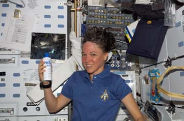 Photo shows a woman with messed hair holding a bottle in front of a panel of instruments.