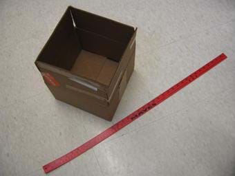 A photograph of 1 foot by 1 foot box with an open top. A red yardstick is laying next to the box.