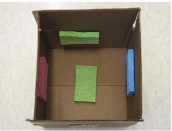 A photograph of 1 foot by 1 foot box with an open top. Sponges (or, sound absorbing panels) have been added to the bottom and sides of the box.