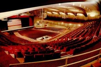 Photo shows the the inside of an auditorium with elevated seats surrounding a stage and acoustical design elements on the walls and ceiling. 