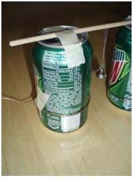 Close up of a soda can, with a wooden dowel taped to the top. with a bell hanging in the middle of the dowel