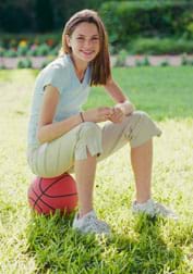 A girl wearing sneakers sits on a basketball.