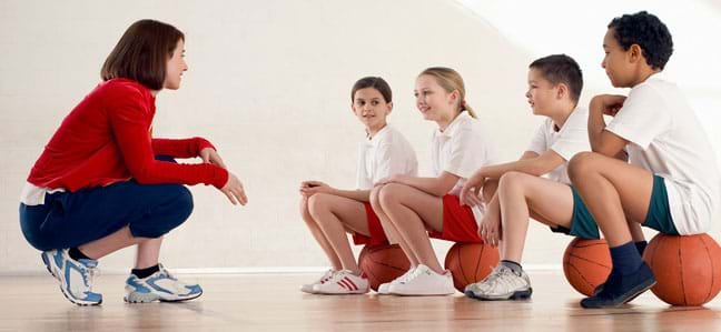 A coach talks to four kids with basketballs - all wearing various kinds of sneakers.