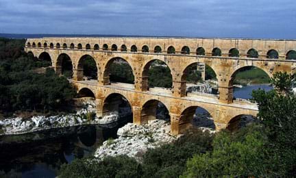 A photograph shows the Roman aqueduct “Pont du Gard” in southern France. It’s a three-layered, multi-arched masonry structure with different-sized arches on each level.