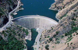 Aerial photo shows an arched-shaped dam blocking a river flow.