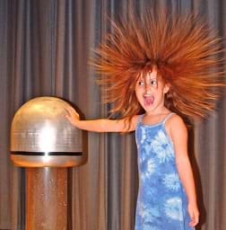 A young girl placing her hand on a Van de Graaff generator causing her hair to rise