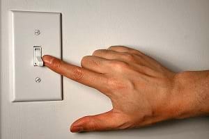 A man placing his finger on an on/off electrical wall switch.
