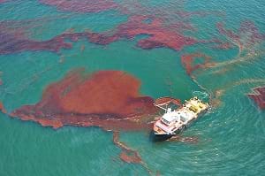 A photo shows a NOAA response and restoration boat near brown gunky masses in the green waters of the Gulf of Mexico from the Deepwater Horizon oil spill.