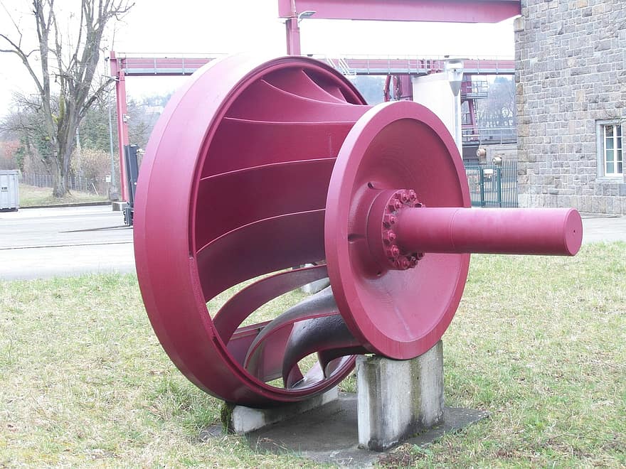 A photo of a large red turbine shaft with curved blades attached like spokes from a hub.