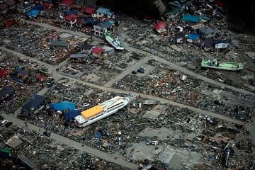 The aftermath of a 9.0 earthquake and tsunami in Japan: A large ferry boat rests inland around destroyed houses.