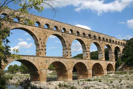 A photograph shows a three-layered, multi-arched Roman masonry aqueduct built across a river. Each level has different-sized arches.