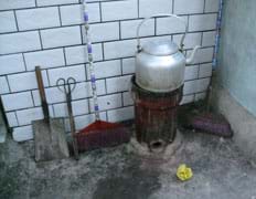 Photo shows a cylinder-shaped stove no wider than the teapot on top. No chimney. Shovels, tongs and brooms lie nearby.