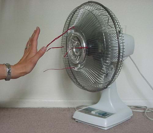 Photograph of a person's hand feeling the moving air in front of a running electric table fan.