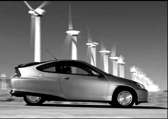 Black and white, side view photograph of a silvery, small, modern-looking car with a row of spinning wind turbines in a line in the background.