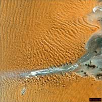 Aerial photo shows waves of orange sand around a river delta.