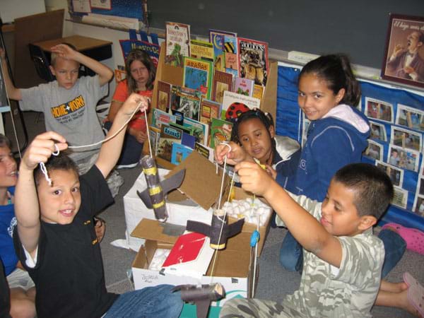 Photo shows seven youngsters around a table with paper, string and construction paper.