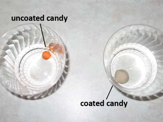 A photo shows an uncoated piece of reddish candy and a whitish coated piece of candy in separate cups of clear soda.