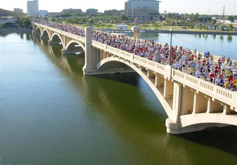 Photos shows mobs of people running a race over a white and graceful concrete bridge. 