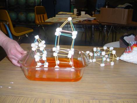 A photograph shows an assembled structure constructed of marshmallows and toothpicks sitting on a bed of orange Jell-O® in a square glass baking dish.