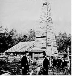 A black and white photo of a tall wooden building with people standing around it.