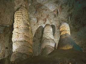 Photograph shows inside of a white stone cave with formations piled up from the floor and hanging down from the ceiling.