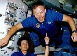 Photo shows one astronaut balancing another astronaut on her pointer finger in microgravity (his chest and body is balanced on her one finger ─ literally!).