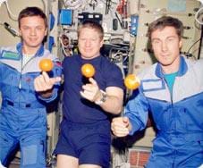 Photo shows three astronauts balancing floating oranges on their right pointer fingers.
