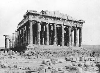 A black and white photograph of the Greek Parthenon, a crumbling structure composed of many columns.