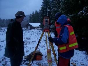 Photo shows a surveyor peering through a theodolite, the optical instrument used for measuring.