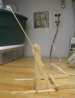 A photograph of a finished catapult. Front and rear stabilizers keep catapult from flipping. A straw is added to the end of the tongue depressor to prevent the grapes from sliding off during launch.