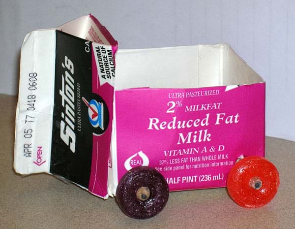 A photograph shows a little vehicle composed of a cut-open milk carton as the cart body with pencil axles and white lifesaver-shaped candy wheels.