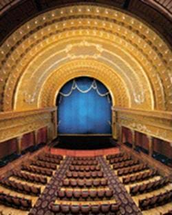 View from balcony of a theater showing curved rows of seats facing a stage with high curved ceiling. 